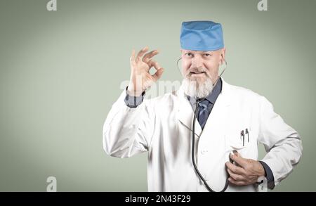 An elderly doctor listens to his heart with a stethoscope and shows ok with a smile. Stock Photo