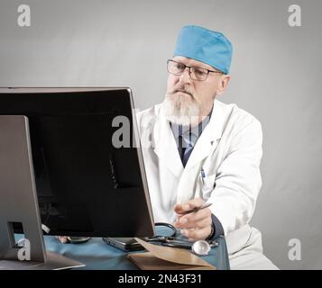 Photo of elderly doctor using prescription laptop, glasses, expert, uniform isolated on gray background. Stock Photo