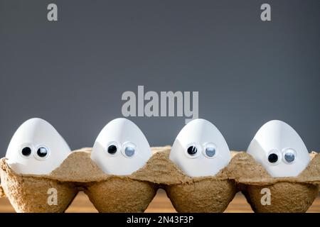 Funny faces on white eggs in carton box with organic chicken eggs on kitchen table closeup big animation eyes. humor, food and easter holiday concept. Stock Photo