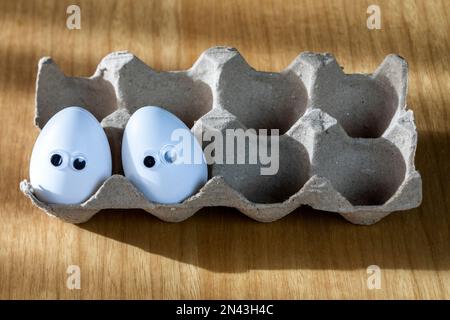 Funny faces on white eggs in carton box with organic chicken eggs on kitchen table closeup big animation eyes. humor, food and easter holiday concept. Stock Photo