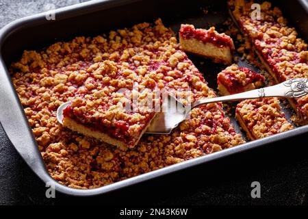 Raspberry Crumble Bars in baking dish on concrete table with cake shovel, close-up Stock Photo