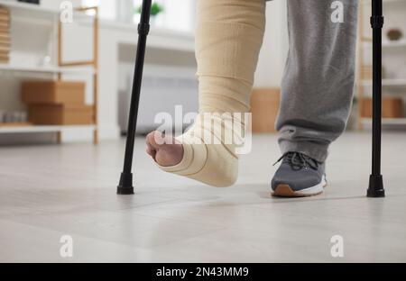 Close up of the feet of a young man with a broken leg walking with crutches at home Stock Photo