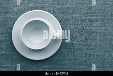 White cup and saucer on natural linen fabric. toned in blue-green, tidewater green. flat lay. space Stock Photo