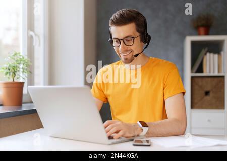 Happy programmer video call with clients and partners. A data center operator works from home. A man wearing glasses and headphones enjoys watching an educational online webinar on his laptop Stock Photo