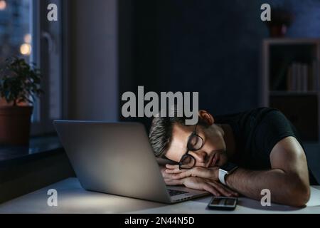 Young overworked distressed businessman freelancer fell asleep at workplace while working remotely overhours, has deadline. Exhausted student sleeping on computer. Work and education failure concept Stock Photo