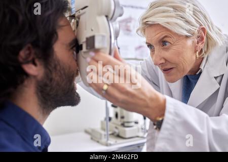 Doctor with a man in vision test or eye exam for eyesight by a focused senior optometrist or ophthalmologist. Optician helping check retina health of Stock Photo