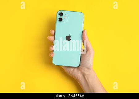 MYKOLAIV, UKRAINE - JULY 10, 2020: Woman holding new modern Iphone 11 Green on yellow background, top view Stock Photo