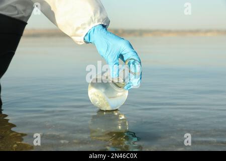 Scientist with florence flask taking sample from river for analysis, closeup Stock Photo