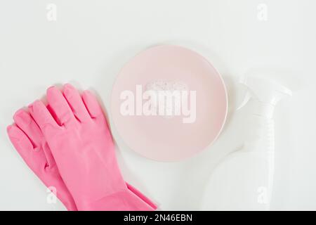 Dish washing concept. Pink gloves, heart shaped foam on plate and white spray bottle. White  background. Flat lay, copy space Stock Photo