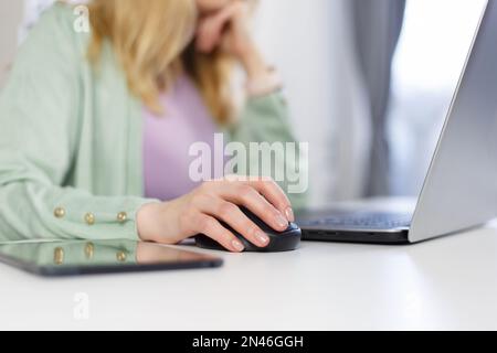 Adult woman working on a computer at home. Unrecognizable white female person clicking with wireless mouse on a laptop Stock Photo