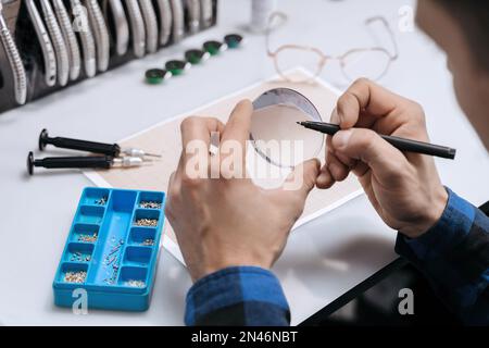 Young professional optometrist is working with lens in optical workshop using special tools and equipment. Vision concept Stock Photo