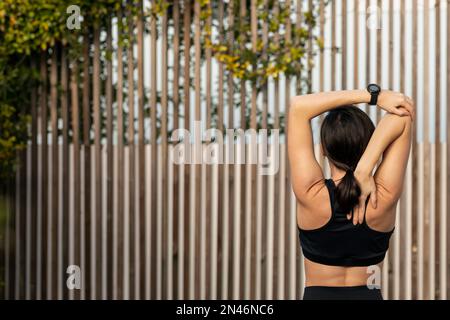 Caucasian millennial muscular slim woman in sportswear doing arm stretching, exercising outdoors Stock Photo
