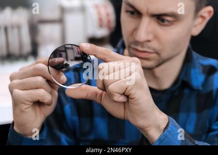 Young professional optician is working with lens in optical workshop using special tools and equipment. Master measuring len, repairing and fixing eye glasses Stock Photo