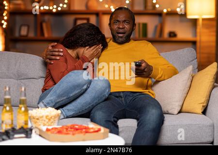 Scared black couple watching horror movie at home Stock Photo