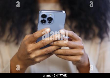 Young black woman typing a message in smart phone app. Close up photo of unrecognizable BIPOC female using modern blue mobile phone for communication Stock Photo