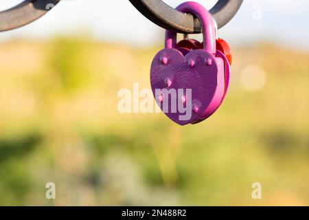 Pink heart shaped lock hangs from bridge chain, wedding custom is symbol of eternal love, copy space Stock Photo