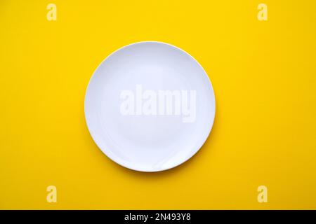 White empty plate with blank surface on bright yellow backdrop, top view Stock Photo