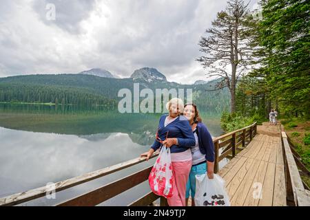 Two women are posing on background of glacial Black Lake in Durmitor National UNESCO park near Zabljak town, Montenegro. Stock Photo