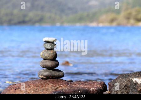 Tower of pebble stones on a beach on background of green mountains. Zen balance, tranquility and travel concept Stock Photo