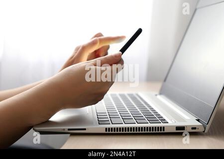 Female hands with smartphone on laptop keyboard background. Woman with mobile phone sitting near the window, concept of online communication Stock Photo