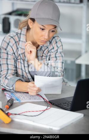 female technician using multimeter and computer and reading instructions Stock Photo