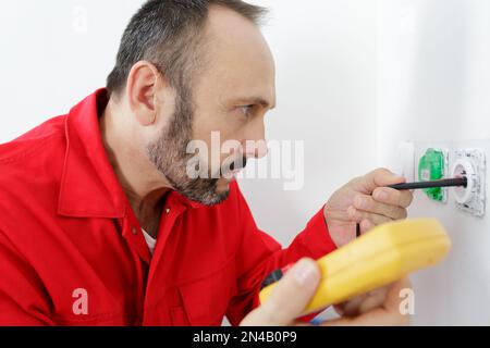 electrician testing plug socket with multimeter Stock Photo