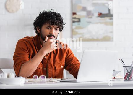 Indian copywriter using laptop near book and notebook on table at home,stock image Stock Photo