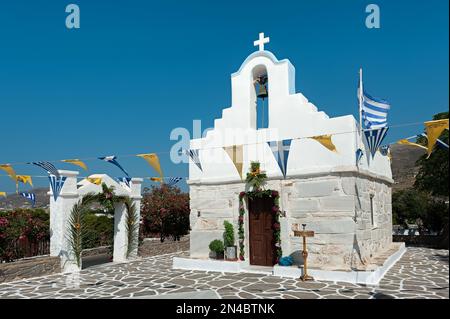 Small church with flower wealth and flags in Parikia, Paros, Cyclades, Greece Stock Photo