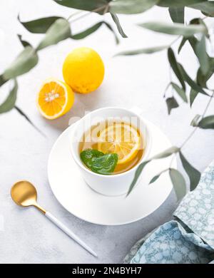 Herbal tea with lemon and mint in a white cup on a light background with eucalyptus branches. The concept of a healthy and delicious breakfast drink f Stock Photo