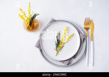 Festive table setting for the spring celebration of women's day, birthday or mother's day with yellow mimosa flowers on a light background with vase. Stock Photo