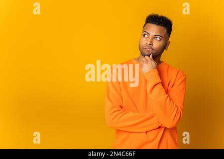 Pensive indian man holding hand near chin and thinking about something, looking for new idea or solution, trying to recall some important thing, puzzled multiracial guy isolated on yellow Stock Photo