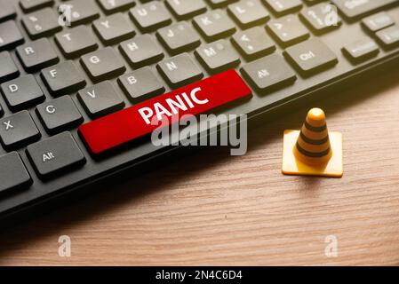 Yellow safety cone and computer keyboard with red button written with PANIC. Stock Photo