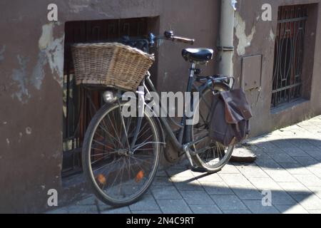 old black bicycle with basket in front leaned on the wall in the street Stock Photo