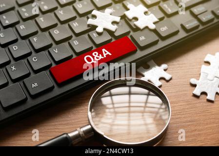 Magnifying glass, jigsaw puzzle and computer keyboard with red button written with QNA or Questions and Answers. Stock Photo