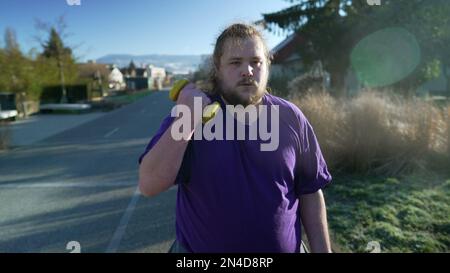 A young fat man getting back into shape building strength. Motivational concept of an overweight person listing weight dumbbells standing outside Stock Photo