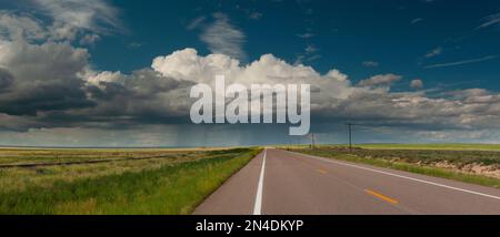 Dramatic storm clouds loom over a rural Nebraska highway, capturing the moody landscape and open road adventure of the American Midwest. Stock Photo