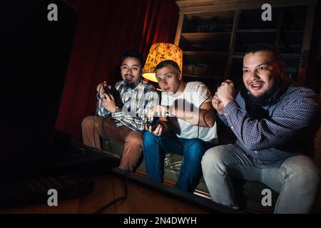 Excited guys play video game on couch at home Stock Photo