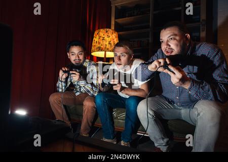 Three high concentrated young guys play video game Stock Photo