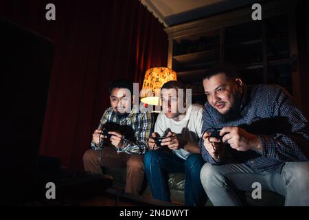 Three concentrated young guy play home video game Stock Photo