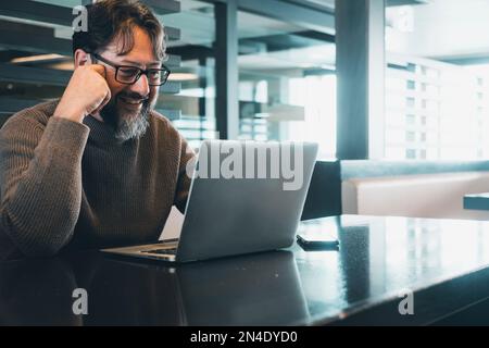 One modern man working on laptop at the desk in empty office or coworking space with light in background. Using computer during travel. Smart lifestyl Stock Photo