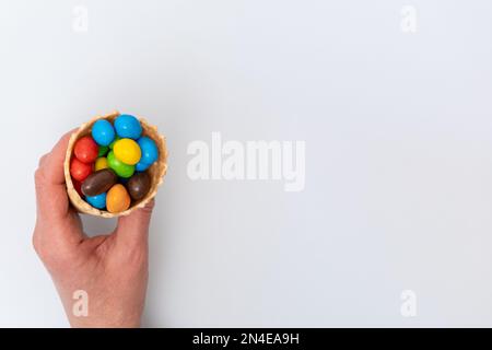 A hand holding an empty waffle cone with scattered multicolored round candies, dragees. A fun holiday. Children's sweets. Stock Photo