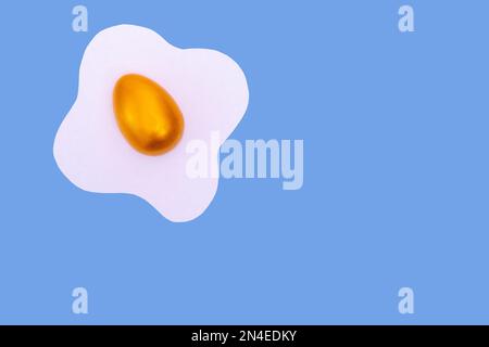 Creative layout made of scrambled eggs with decorated golden Easter eggs on a blue background. Minimal Spring holidays concept. Stock Photo