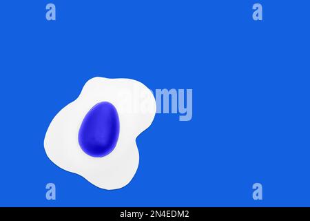 Creative layout made of scrambled eggs with painted blue half Easter eggs on a blue background. Minimal Spring holidays concept. Stock Photo