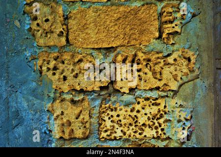 Old yellow wall of limestone with natural holes and grey cement seams, close-up view. Stock Photo