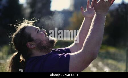 Religious young man raising arms in the air feeling the presence of God. Dramatic person raising hands into sky asking for help Stock Photo