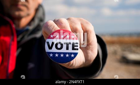 Man is holding patriotic button with Vote text outside Stock Photo