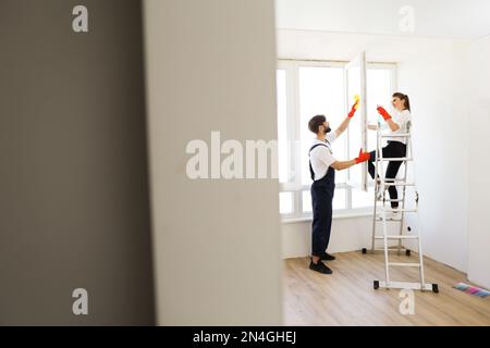 Beautiful caucasian couple wife and husband cleaning window together in room. Hard working family use spray while washing window, working together. Stock Photo