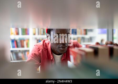 Black student man choose book in college library learning in university preparing for test or exam Stock Photo