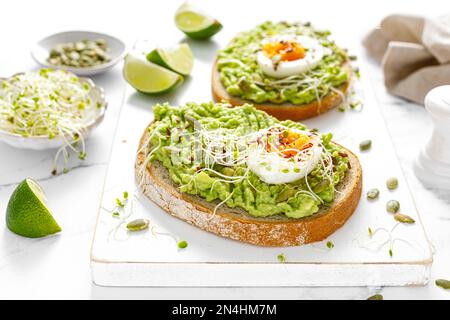 Avocado toast with boiled egg, seeds and sprouts on white background. Healthy diet food Stock Photo