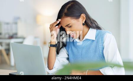 An overworked business woman with a headache while working in her office. A tired or stressed corporate female in pain at the workplace. A young Stock Photo